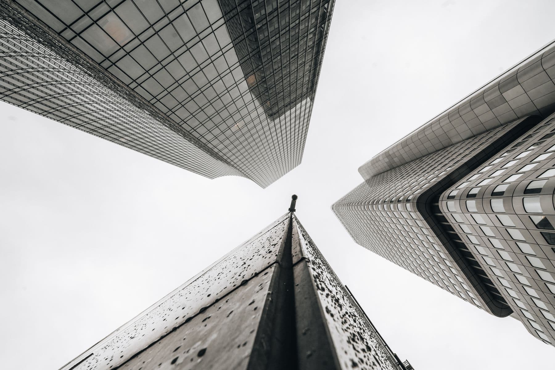 Looking straight up between towers of glass and stone against a pale sky